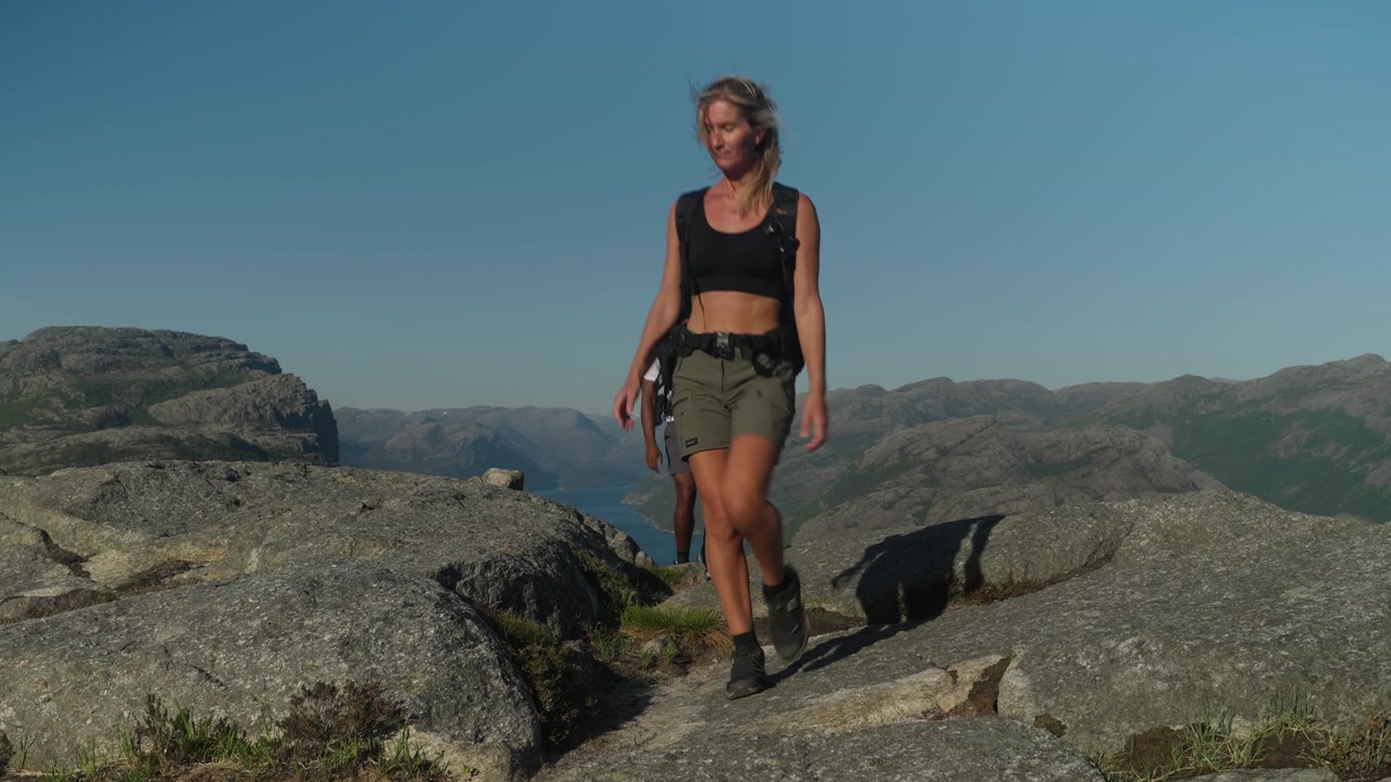 Sportliches Paar wandert auf einen felsigen Granitberg in Norwegen mit atemberaubenden Fjordblicken, klarem blauem Himmel und schönen Sommerbedingungen in einer malerischen nordischen Landschaft