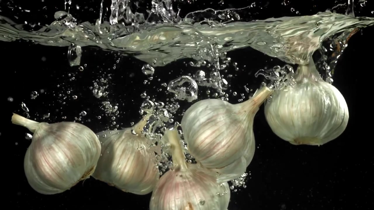 Bulbi d'aglio freschi che cadono nell'acqua al rallentatore