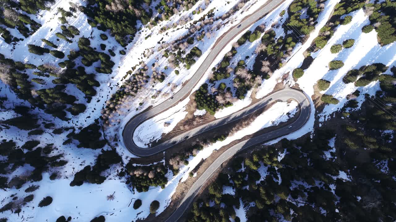 Aerial top-down view of the winding Maloja Pass road cutting through a snowy alpine forest, showcasing sharp curves, winter landscape, and scenic mountain travel route