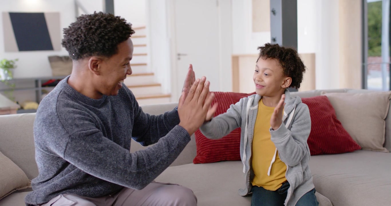 African American father and daughter starting clapping game on light sofa with red pillows, bonding