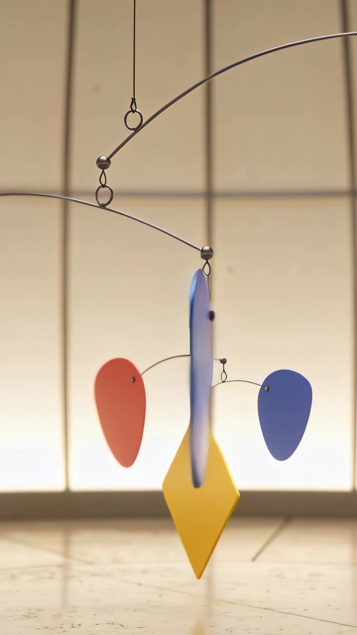 Vertical video: Swaying kinetic mobile being nudged by soft air in studio, showing yellow diamond