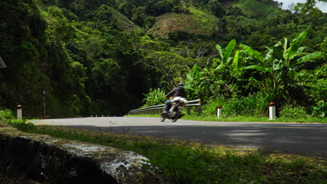 Tourists-on-a-Motorcycle-Riding-the-Ridge-Parkway-in-the-Mountains-near-Phan-Rang,-Da-Lat-during-the-Summer-with-Rock-Stone-Walls-and-Green-Trees-Around-them