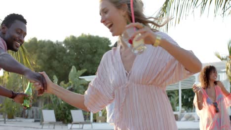 Happy-diverse-group-of-friends-dancing-holding-cocktails-at-beach