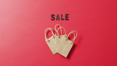 sale in black letters with three brown gift bags on red background with copy space