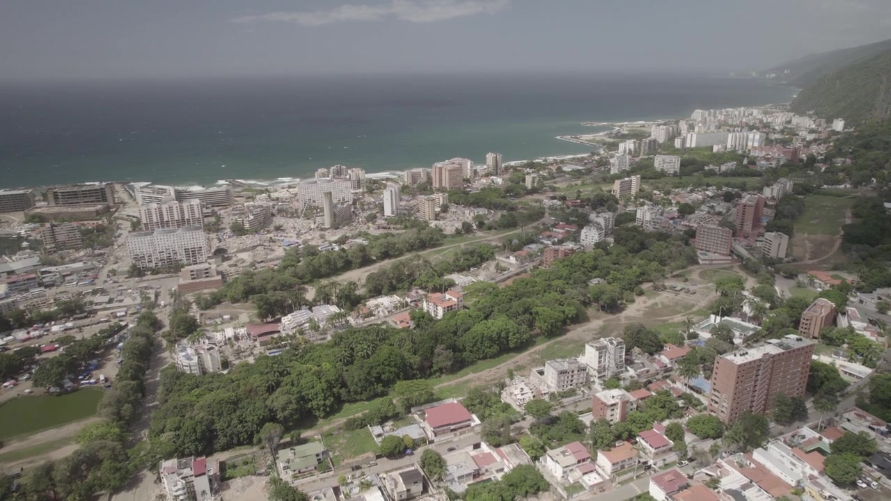 Prospettiva aerea da drone che documenta l'estensione spaziale dei danni del terremoto nella città costiera caraibica di La Guaira, Venezuela. Campi da golf verdi in contrasto con edifici crollati