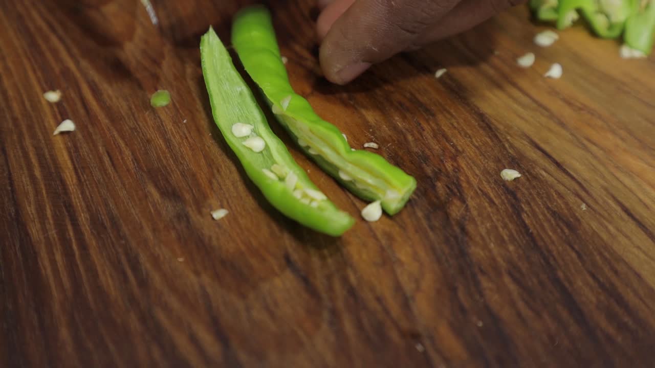 toma de mano - primer plano de las manos cortando chile verde en una tabla de madera - cortando verduras en trozos pequeños con un cuchillo - concepto de comida saludable