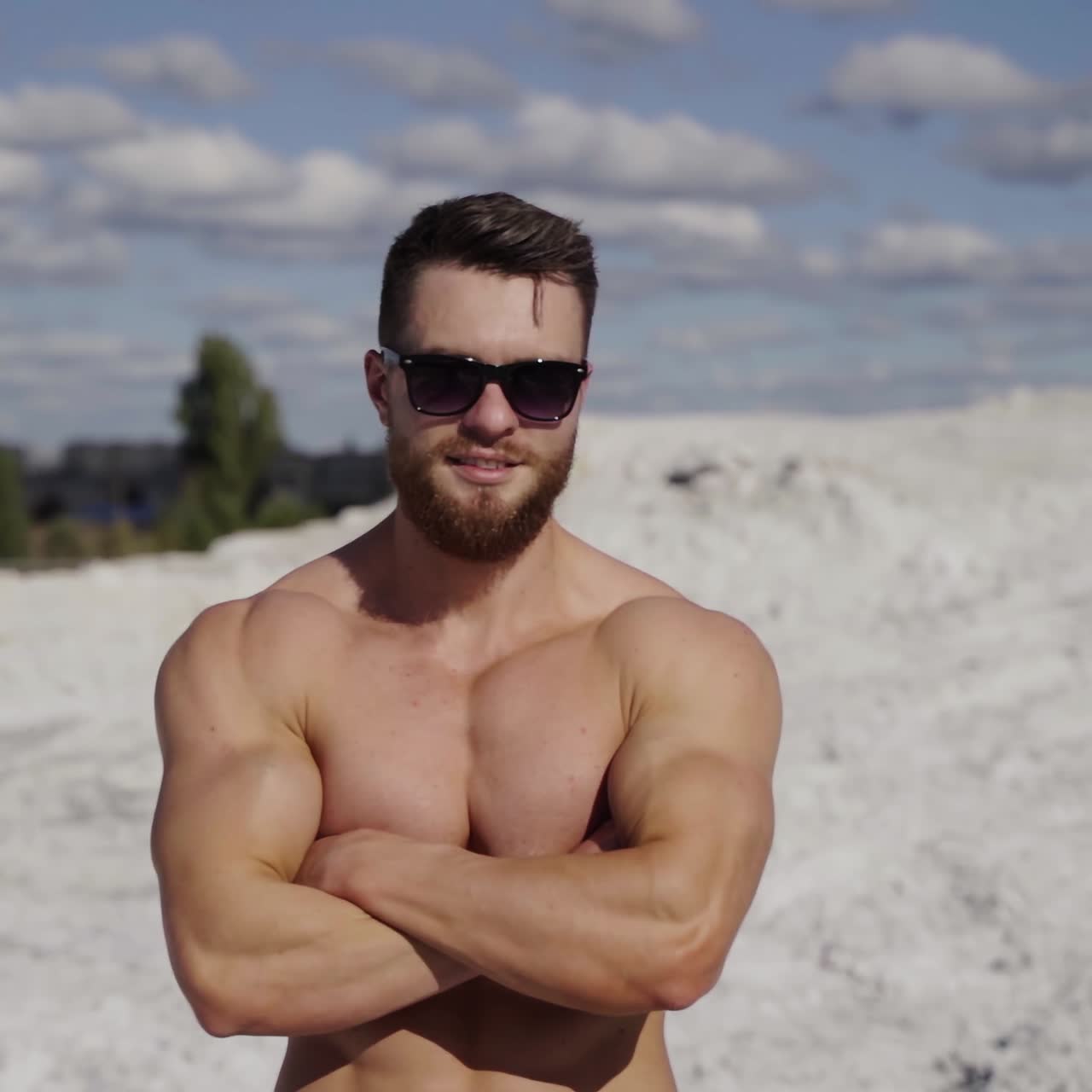 Portrait of shirtless athlete. Handsome guy with beard in sunglasses with muscular body posing on white canyon in summer. Camera motion around.