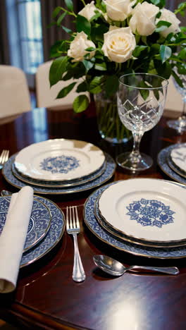 elegant dining table setting with white roses and blue patterned dinnerware