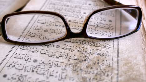 Footage of an old Quran and glasses lying on it, the shot moves away