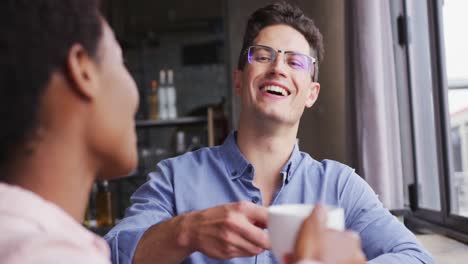 two happy diverse male and female friends sitting in cafe drinking coffee, talking and laughing
