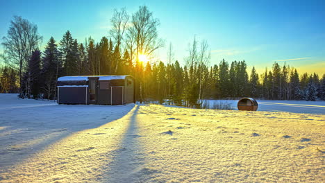 Beautiful-yellow-sunrise-in-a-blue-sky-over-a-snowy-meadow-with-chalet