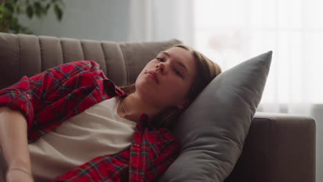 Thoughtful-young-woman-in-casual-clothes-dreams-on-sofa