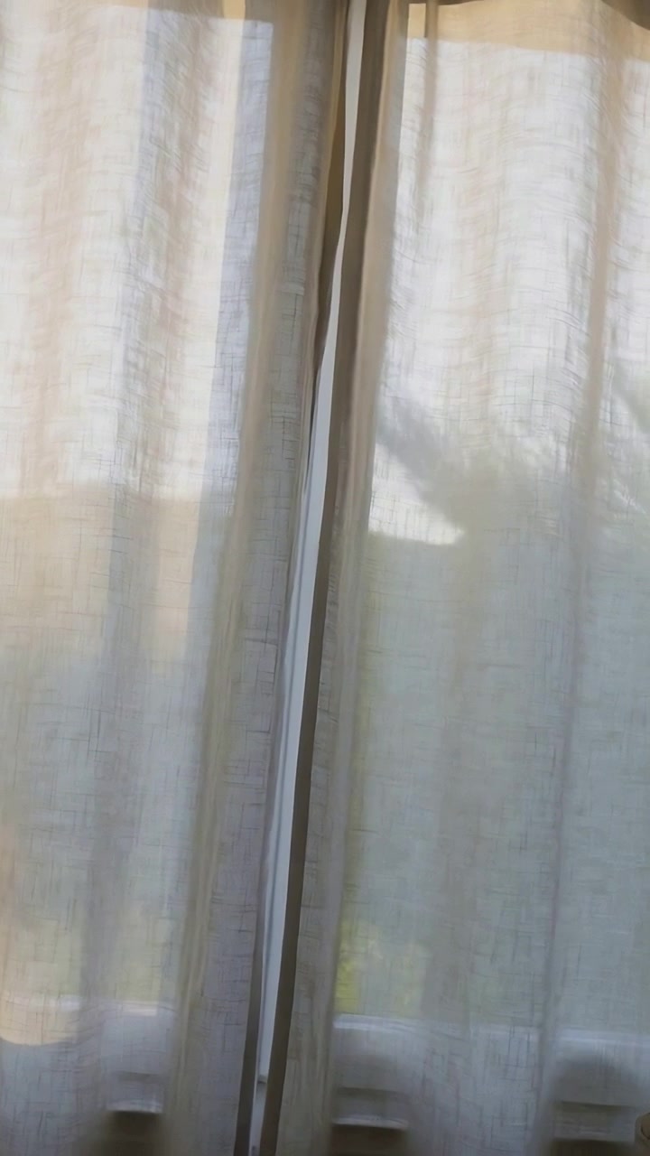 Vertical video: Tilting cam centering seam while sun shifting through sheers in room, seeking light
