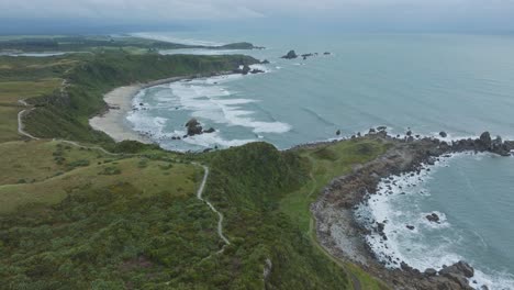Scenic-aerial-view-of-coastal-landscape-with-long-winding-pathway-overlooking-the-Tasman-Sea-at-Cape-Foulwind-on-West-Coast,-South-Island-of-New-Zealand-Aotearoa
