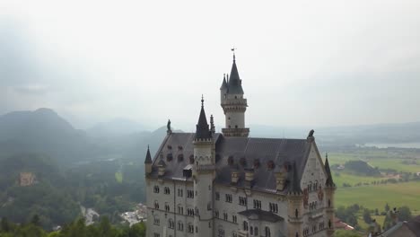 aerial orbit of fairytale neuschwanstein castle on a hill surrounded by woods, pollat river and village in background on an overcast day, bavaria, germany