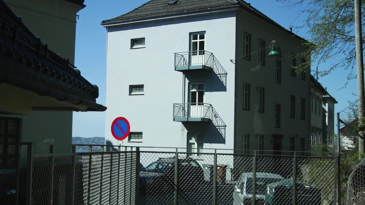 Ohitetaan asuinrakennuksia ja aidattu pysäköintialue aurinkoisena päivänä Bergenissä.