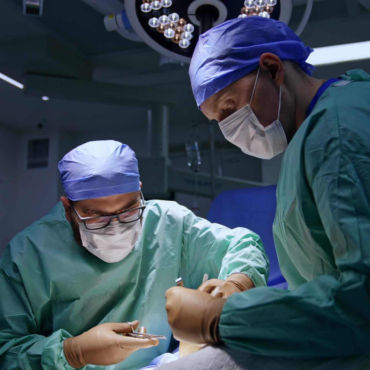 Focused chief surgeon bent over the patient using metal tools. Assisting doctor holds the instrument to help the colleague