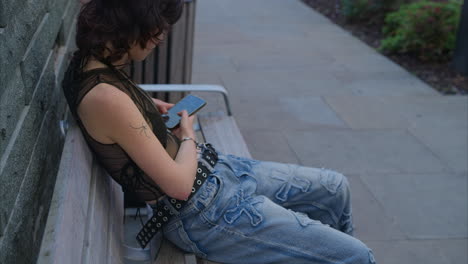 Outdoor-Fashion-Portrait-Of-Young-Alternative-Style-Woman-With-Tattoos-Sitting-On-Bench-Messaging-On-Mobile-Phone