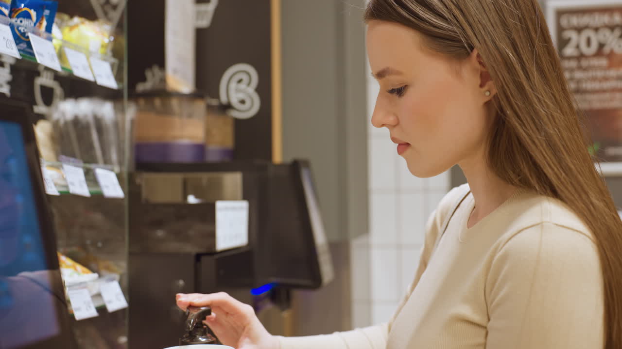 Giovane donna che riempie una tazza di caffè da asporto al chiosco self-service nell'area casse del supermercato, seleziona la dimensione e preme l'erogatore, illuminazione ambientale calda, scaffali e menu a vista sullo sfondo, abbigliamento casual