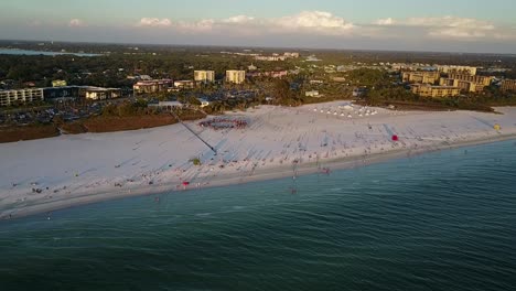 aerial shot, slow approach to scenic white sandy beaches over turquoise water on siesta key beach florida with drum circle