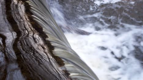 closeup on small flowing copper woodland reflections river cascading into waterfall left dolly slow