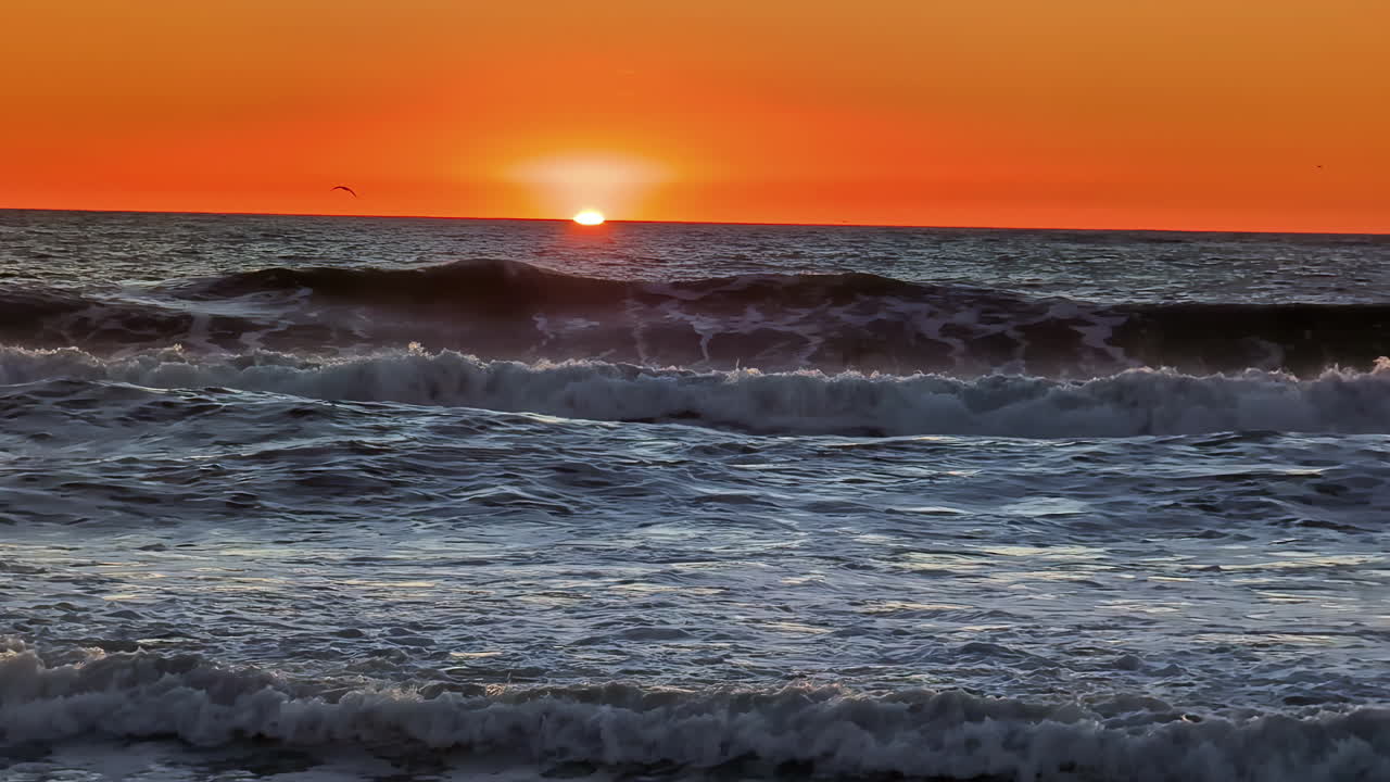 저녁 시간 에 모래 해변 을 따라 파도 가 부히는 지평선 위 의 오렌지색 하늘 을 따라 장엄 한 해 가 지는 모습 의 타임 스