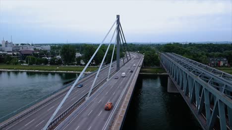 drone slowly descents next to a bridge spanning a river while cars and trucks pass by in central europe