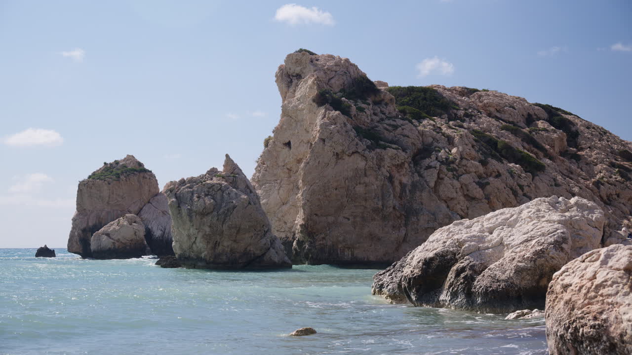 Large natural rock formations rising from the sea at Aphrodite's Rock, a famous coastal landmark in Cyprus. Clear blue water and bright sky highlight the rugged Mediterranean landscape