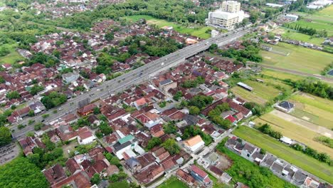 Highway-road-and-Yogyakarta-outskirts-surrounded-with-green-rice-fields,-aerial-view