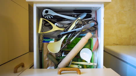 kitchen draw full of messy utensils is opened, left open, and then closed