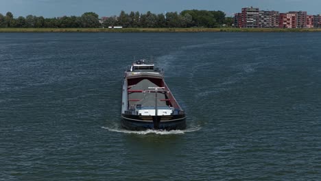 cargo barge travels on river near urban development under blue sky