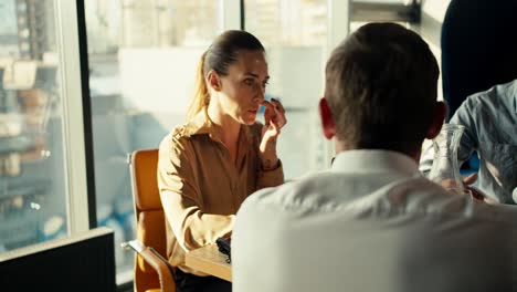 mujer adulta gerente rubia se comunica en una reunión de empleados de la oficina en la mesa. oficina con ventanas panorámicas
