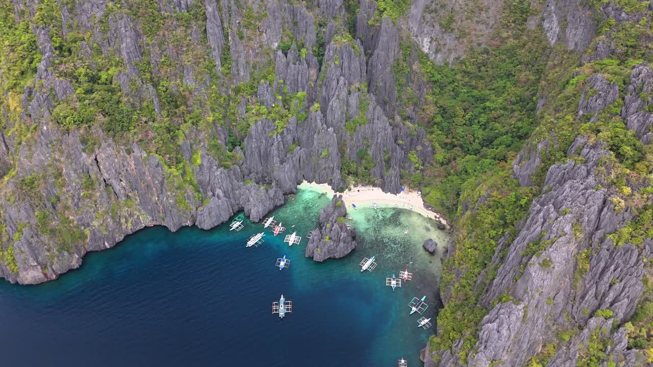 Aerial view of Secret Lagoon and Jiji's Beach on Miniloc Island, Philippines, featuring limestone cliffs, lush forest, white sand beach, and traditional boats on vibrant turquoise water