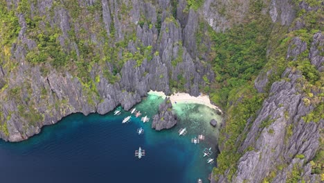 aerial view of secret lagoon and jiji's beach on miniloc island, philippines, featuring limestone cliffs, lush forest, white sand beach, and traditional boats on vibrant turquoise water