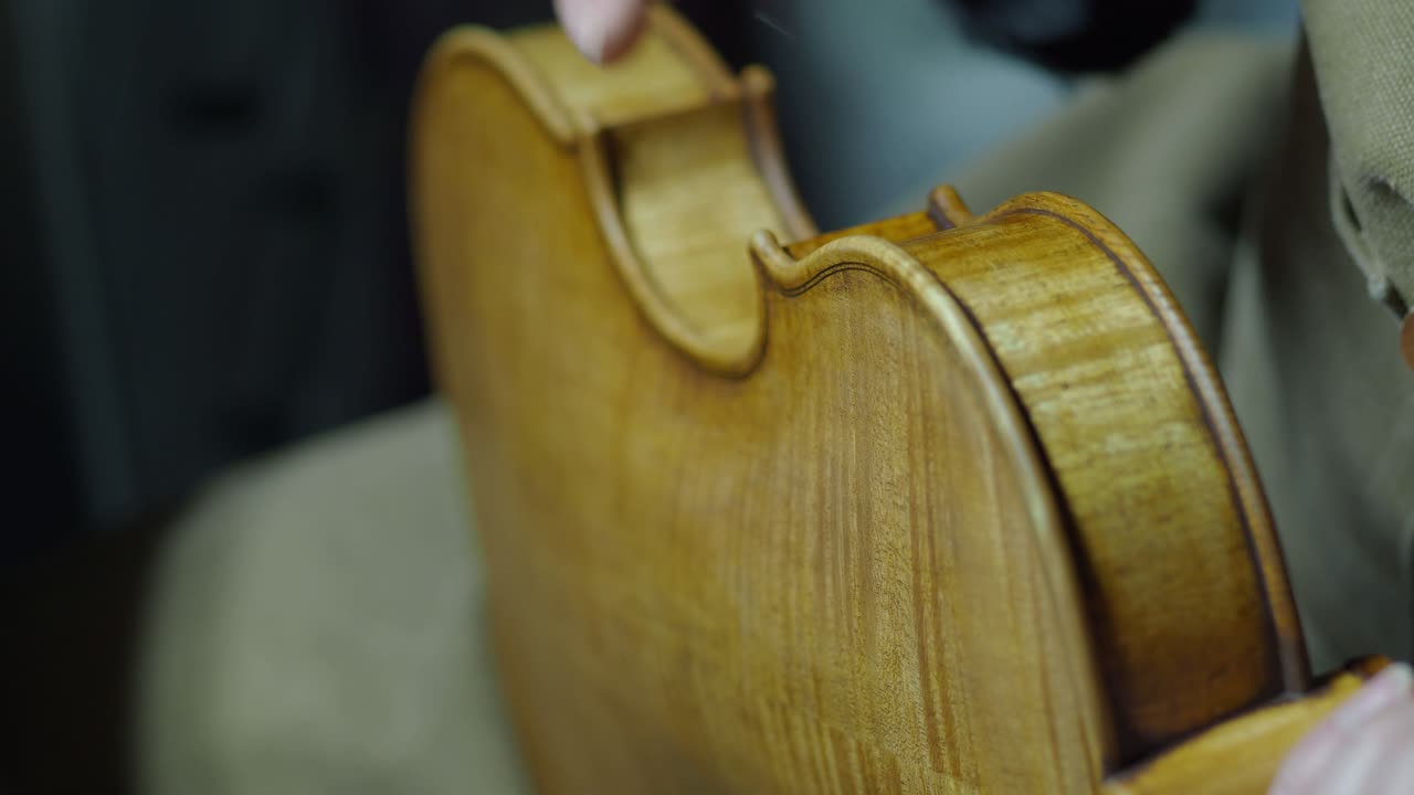 Liutaio applica smalto colorato e patina alle fasce del violino per replicare invecchiamento e usura, parte del processo di verniciatura anticante, con venatura del legno visibile. Primo piano macro a mano libera, tecnica del pennello