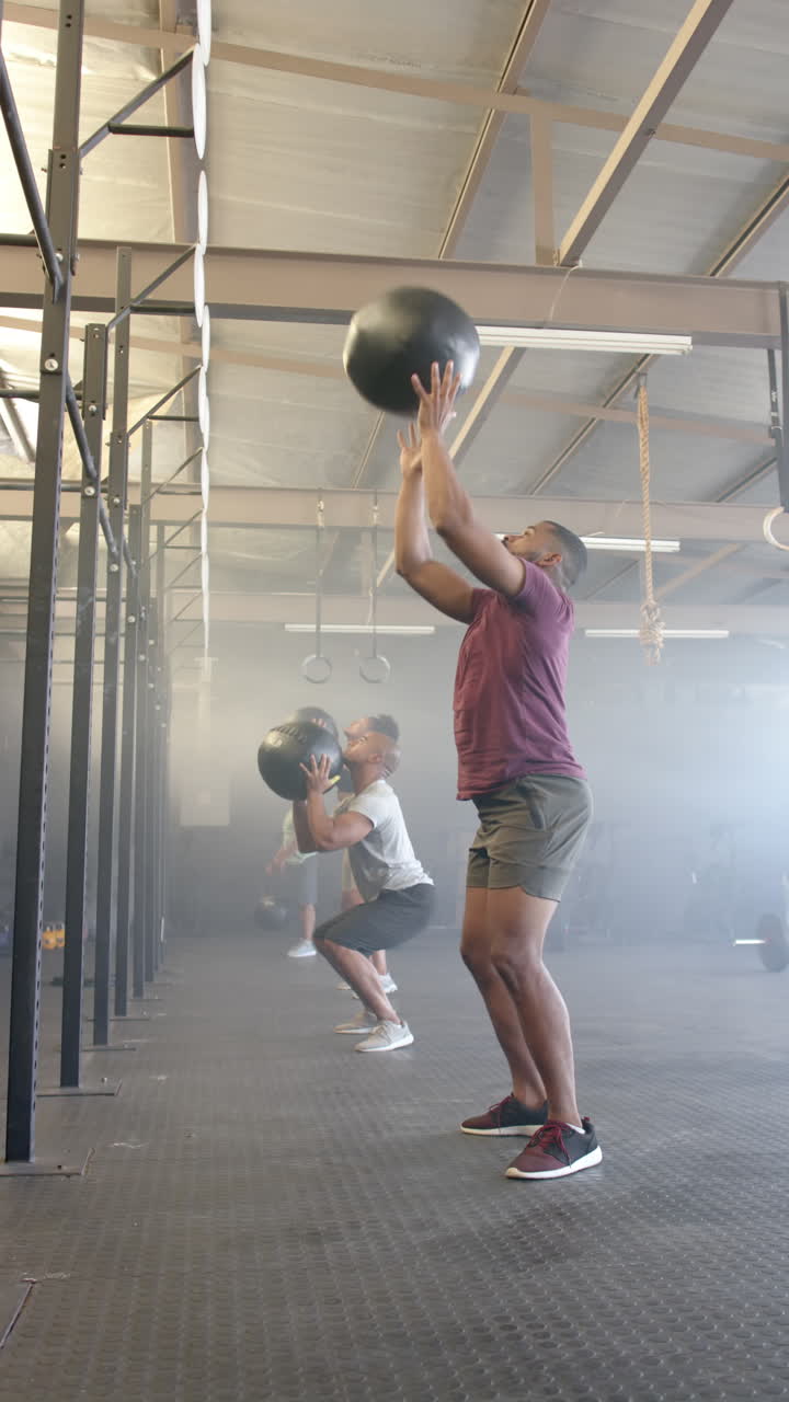 Vertical video of diverse sports people lifting medicine balls at gym in slow motion