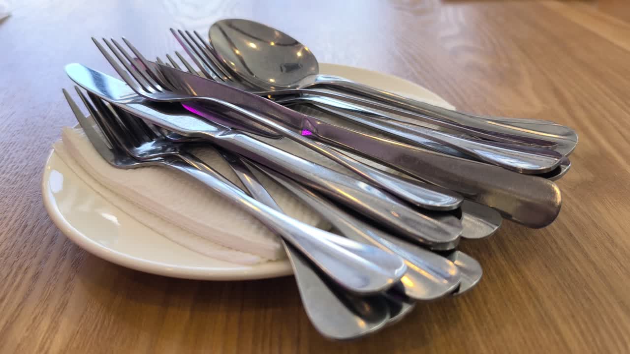 Clean silverware rests neatly on a white plate and napkin. The cutlery is set on a dining table. Everything is ready for the upcoming meal service
