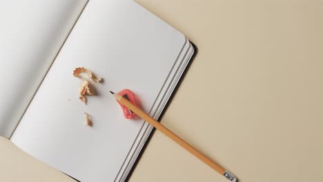 overhead view of open notebook with pencil and pencil sharpener on beige background, in slow motion