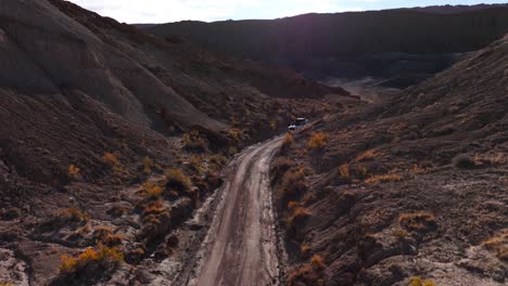 descending aerial white off road suv driving on dirt road through desert landscape