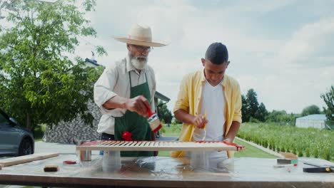 grandfather and grandson painting wooden planks outdoors