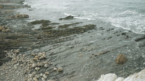 UHD-waves-coming-in-over-rocky-dark-beach-on-overcast-summer-day