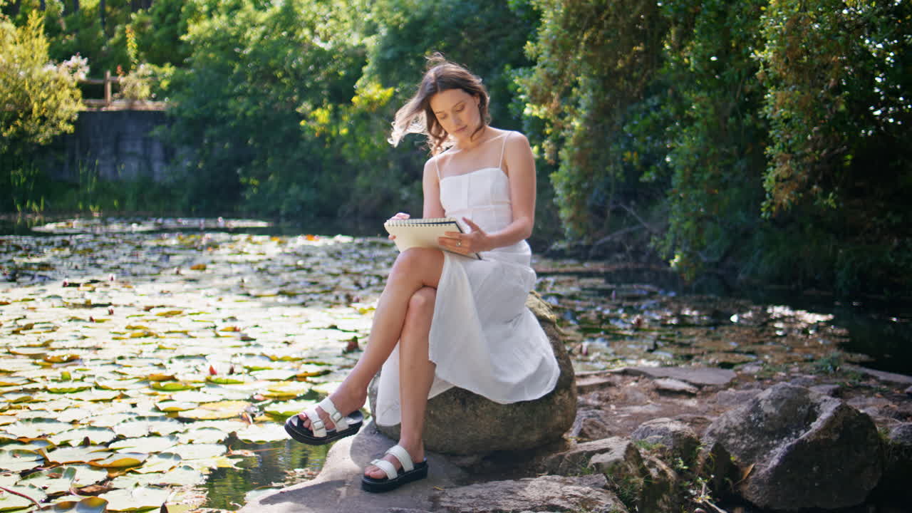 Romantic artist sketching album relaxing at wild forest landscape. Woman drawing