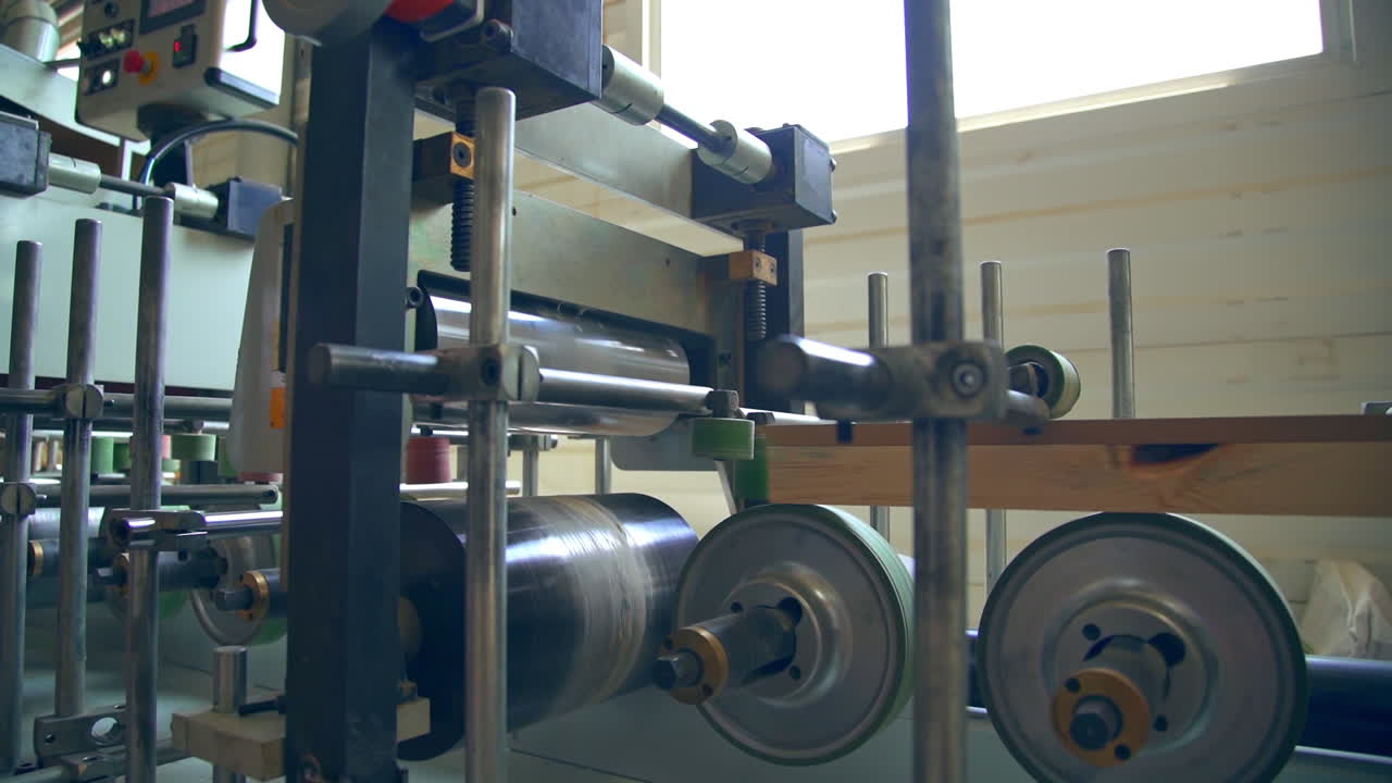 Automatic equipment at modern woodworking factory. Wooden bar moving quickly along the line due to rotating shafts.