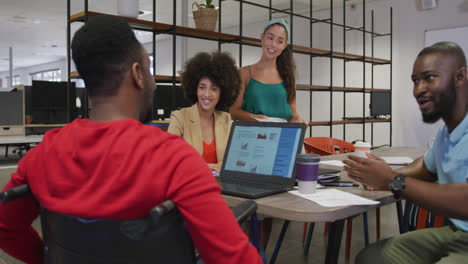 diverse male and female business colleagues and disabled businessman talking and using laptop