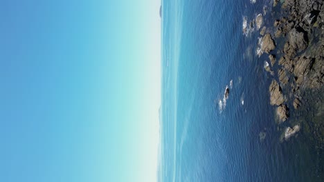 vertical video of rocky coastline in sanxenxo flyover calm seascape and blue sky, galiza