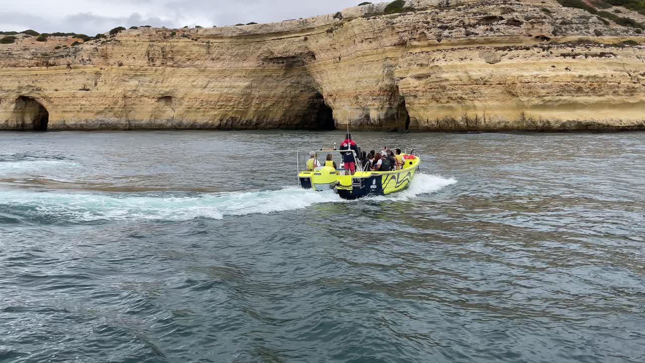 Motoscafo che naviga lungo la costa del Portogallo, con scogliere e grotte marine sullo sfondo