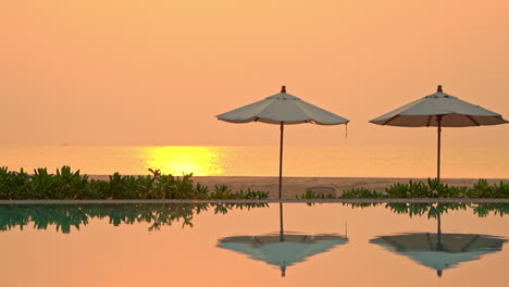 Serene-caribbean-summer-evening-scenery,-poolside-with-umbrella-reflection-and-yellow-sunlight-on-sea