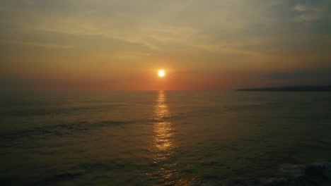 Aerial-seascape-view-of-waves-crashing-on-a-tropical-coastline-wiht-palm-trees-silhouettes,-at-sunset