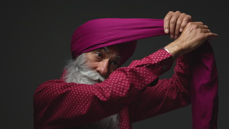 close up low key studio lighting shot de un anciano sikh con barba usando aguja salai cuando se pone el turbante contra un fondo oscuro shot en tiempo real 1