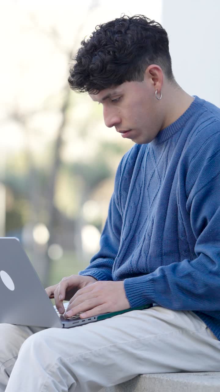 Young man experiencing headache while working on laptop outdoors. Vertical